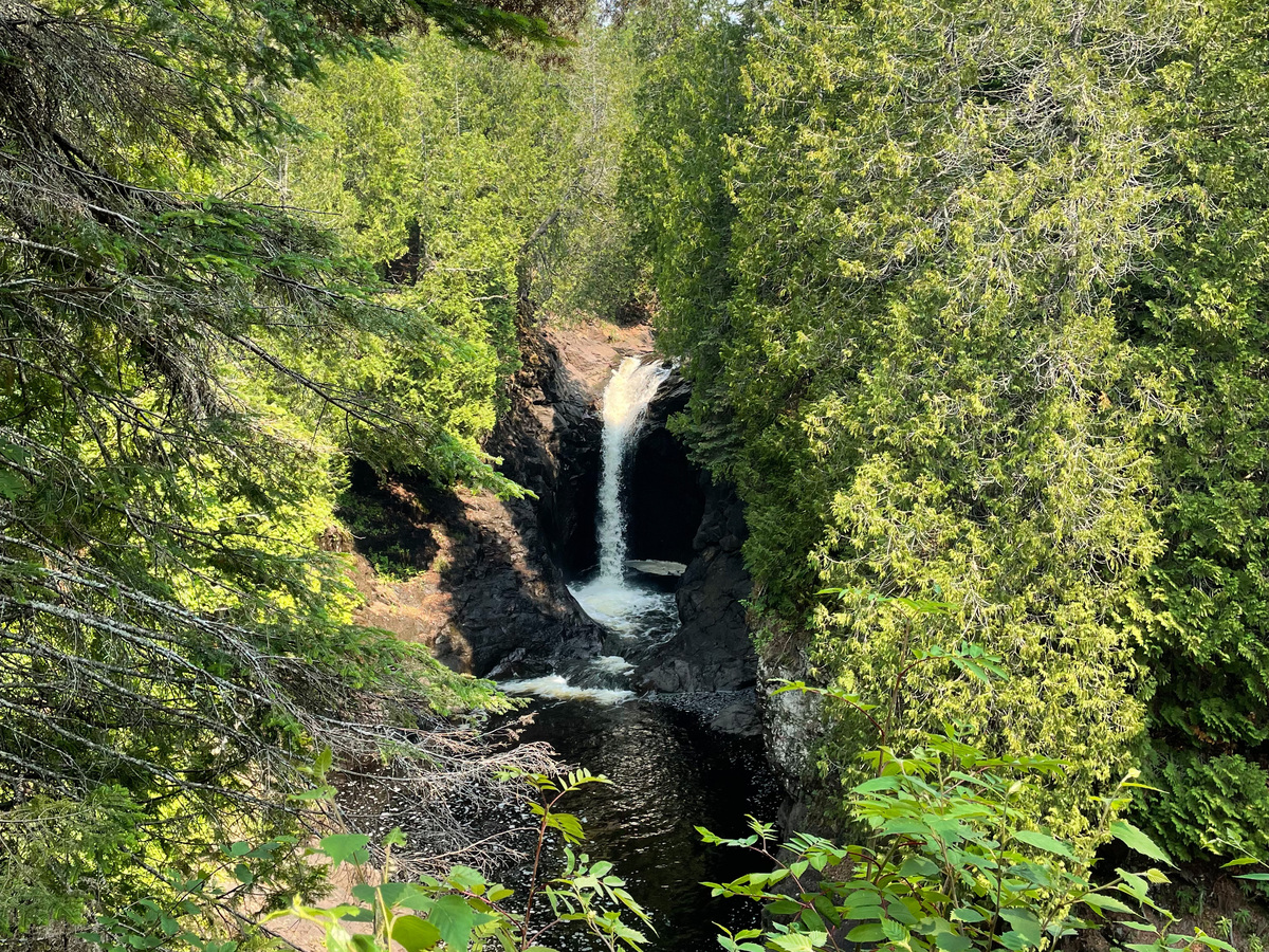The waterfall at Cascade River State Park through verdant trees.