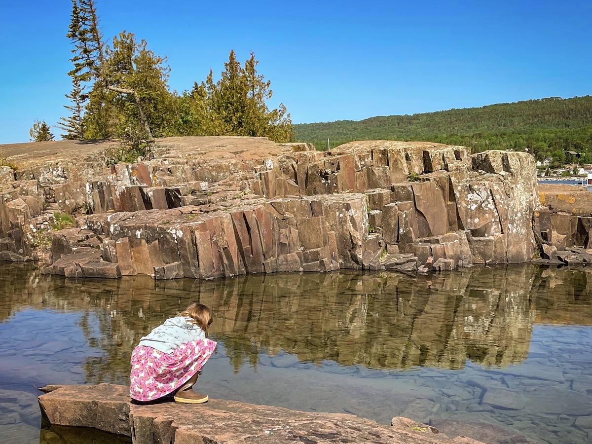 A young girl leans over to splash in a small rock pool near the lighthouse in Grand Marais.