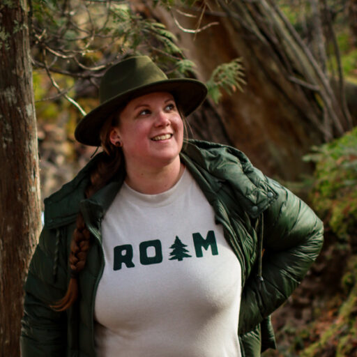 Antonia in the woods with a sweatshirt reading "ROAM".