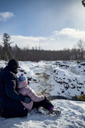 A man and his daughter look at a frozen waterfall in Ely.