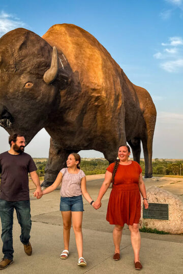 A family of three walks together in front of Jamestown's World's Largest Buffalow.
